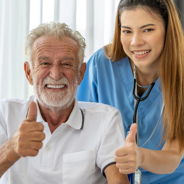 Happy elderly senior man in wheelchair with happy nurse, both with thumbs up